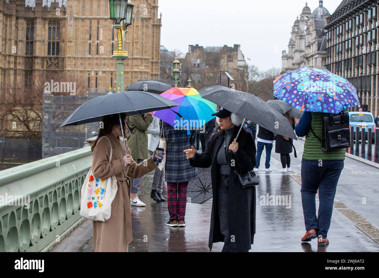 London, UK, 13. Februar 2024 Touristenwarteschlange im Regen mit Regenschirmen, um Fotos von der ikonischen Red Phone Box in London zu machen und die Sehenswürdigkeiten in London trotz Regen zu genießen Credit: Richard Lincoln/Alamy Live News Stockfoto