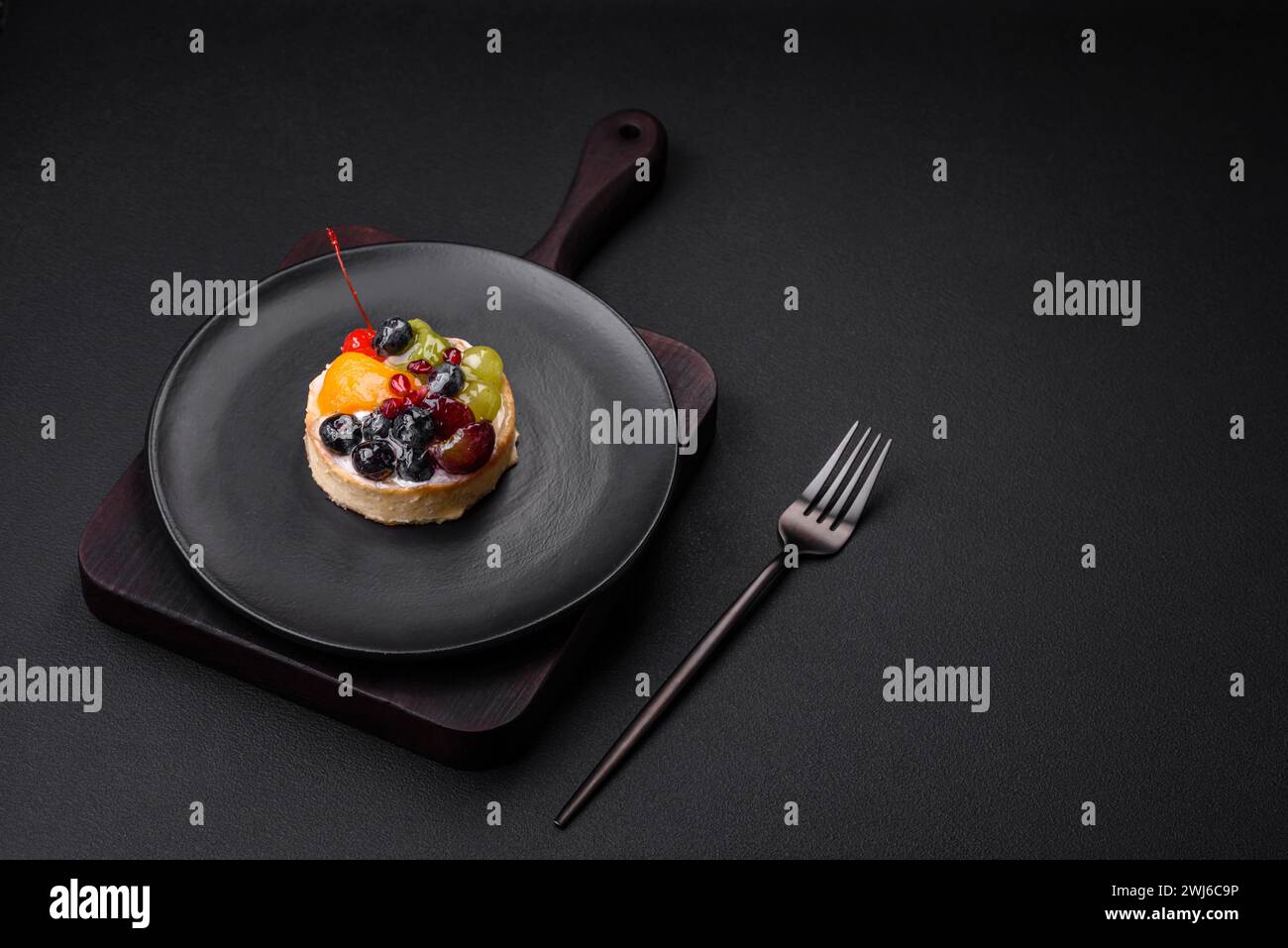 Köstliche frische Tarte mit Heidelbeeren, Kirschen, Trauben auf einer schwarzen Keramikplatte Stockfoto