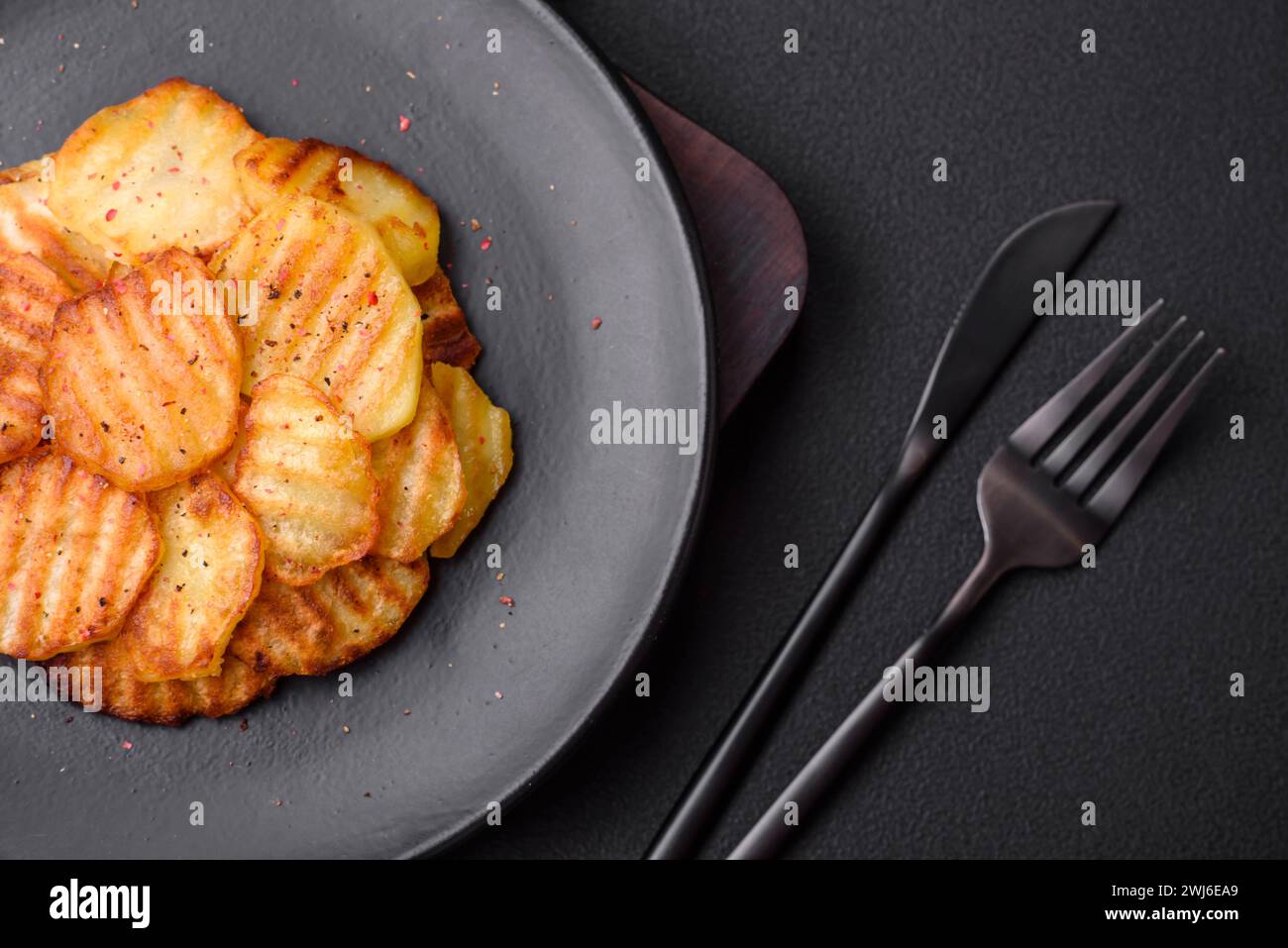 Köstliche knusprige Bratkartoffeln in Scheiben auf einer schwarzen Keramikplatte Stockfoto