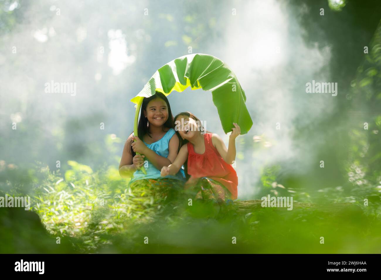 Zwei asiatische Mädchen mit traditionellem Bekleidungsstand hatten Spaß beim gemeinsamen Spielen im Regenwald. Stockfoto