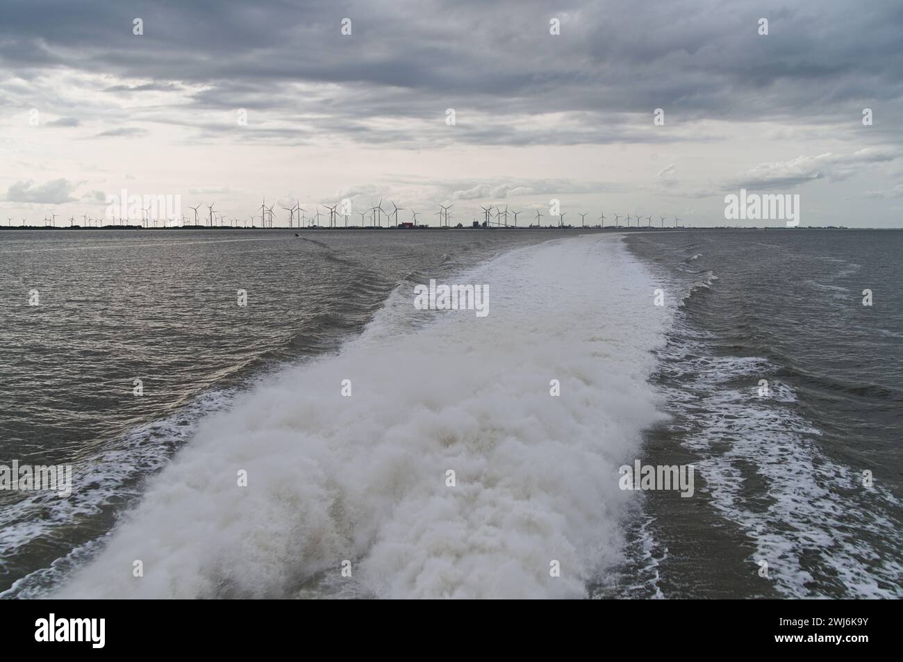 Blick hinter das Meer zu vielen Windturbinen mit den Wellen des Bootes in der Nähe von Borkum Stockfoto