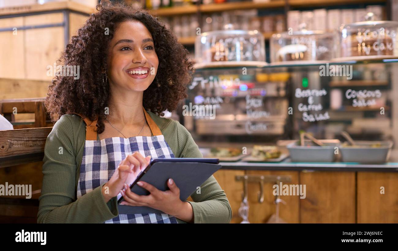 Lächelnde Junge Frau Mit Schürze, Die Im Lebensmittelgeschäft Mit Einem Digitalen Tablet Arbeitet Stockfoto