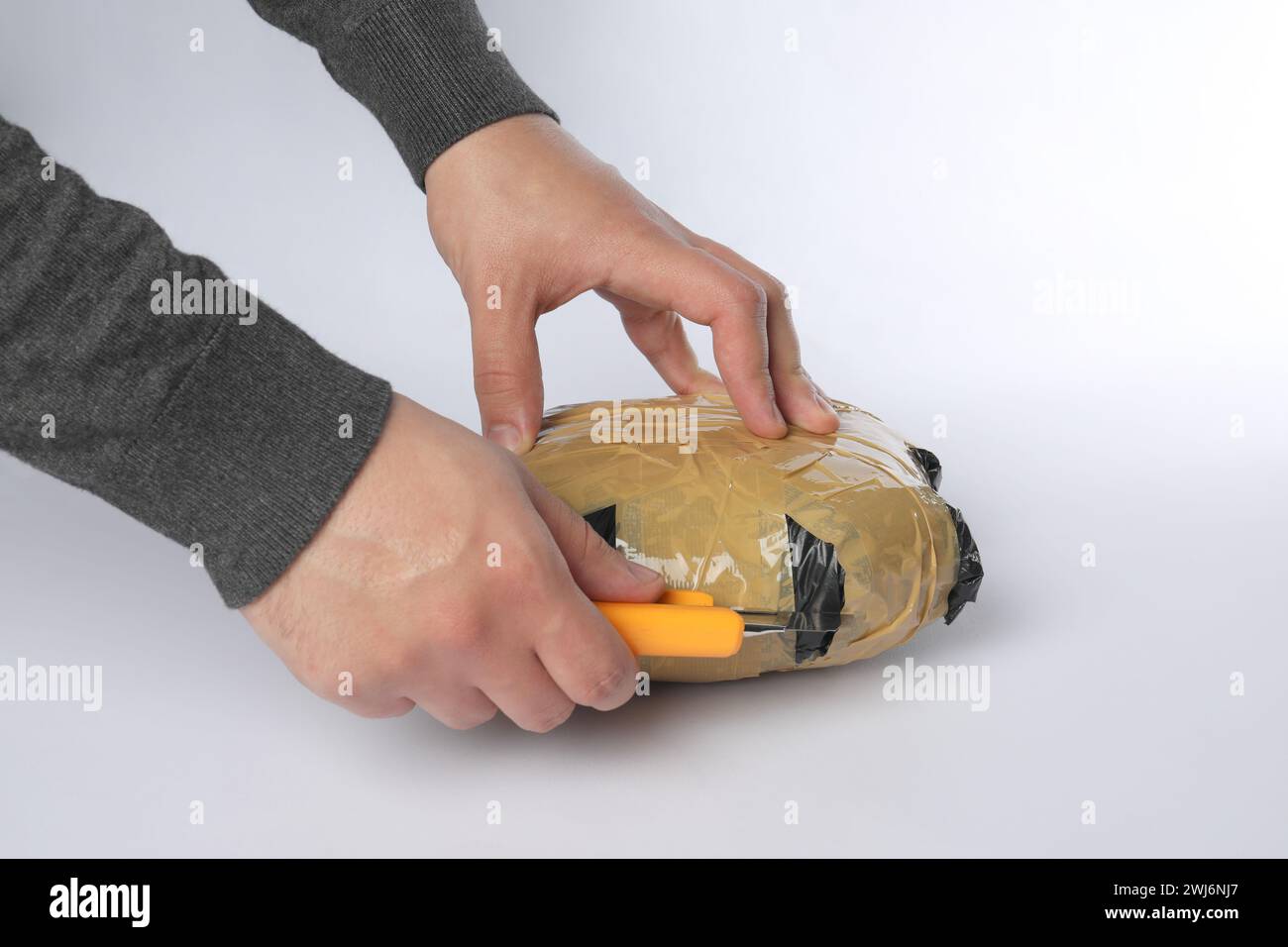 Schmuggel und Drogenhandel. Mann, der ein Paket mit Betäubungsmitteln mit einem Koffer auf weißem Hintergrund öffnet, Großaufnahme Stockfoto