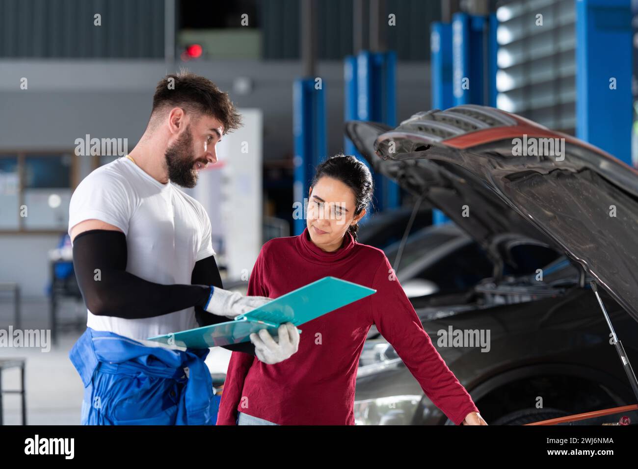 In einer Autoreparaturwerkstatt informiert Ein professioneller Automechaniker eine Kundin über die Kosten für Autoreparaturen und holt ihr Geld ein Stockfoto