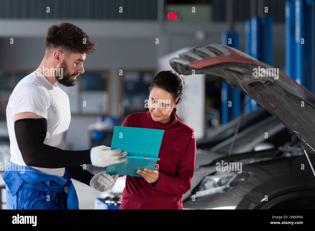 In einer Autoreparaturwerkstatt informiert Ein professioneller Automechaniker eine Kundin über die Kosten für Autoreparaturen und holt ihr Geld ein Stockfoto