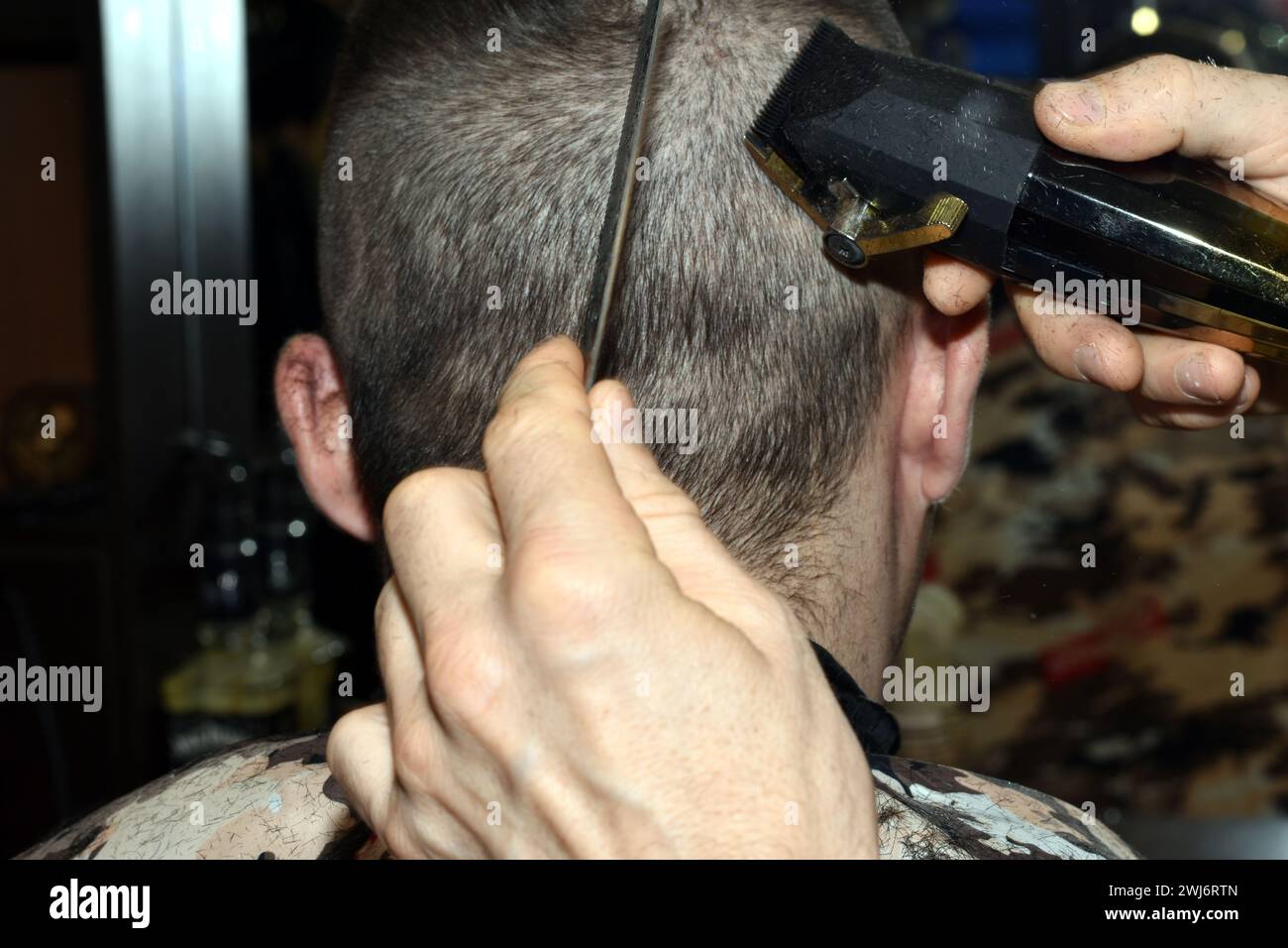 Haare schneiden in einem Salon am Kopf eines Mannes. Ein Friseur verwendet eine elektrische Maschine und einen Kamm, um Haare von der Rückseite des Kopfes des Kunden zu entfernen. Stockfoto