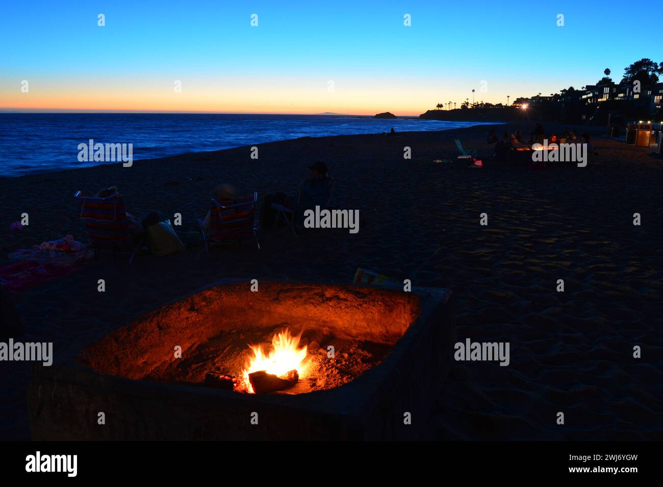 Die Menschen versammeln sich an einem offenen Lagerfeuer an der Küste, während die Sonne über dem Pazifik am Laguna Beach, Kalifornien, untergeht Stockfoto