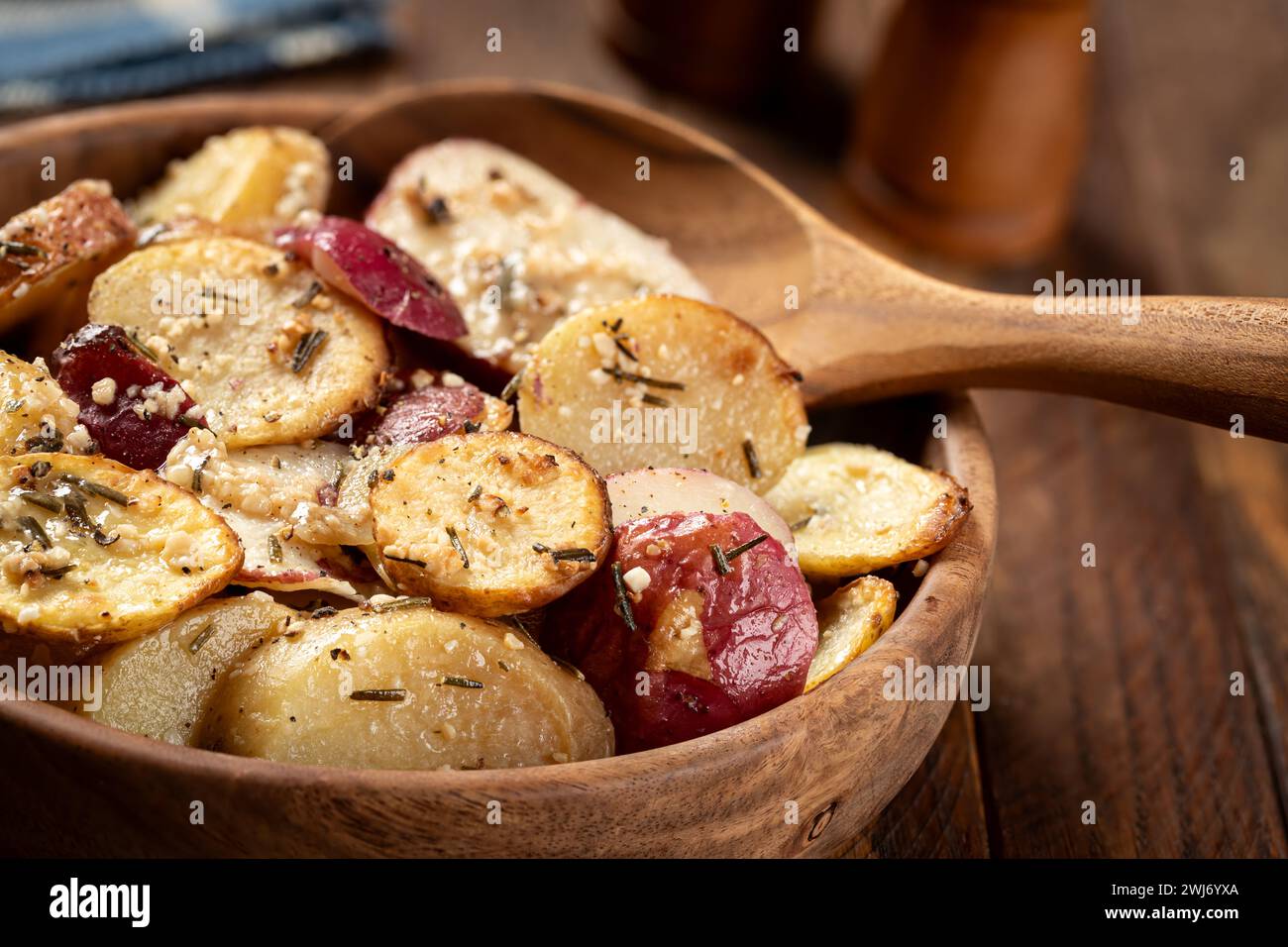 Nahaufnahme von gebratenen Kartoffeln, gewürzt mit Rosmarin und Knoblauch in einer Holzschale auf einem rustikalen Tisch Stockfoto