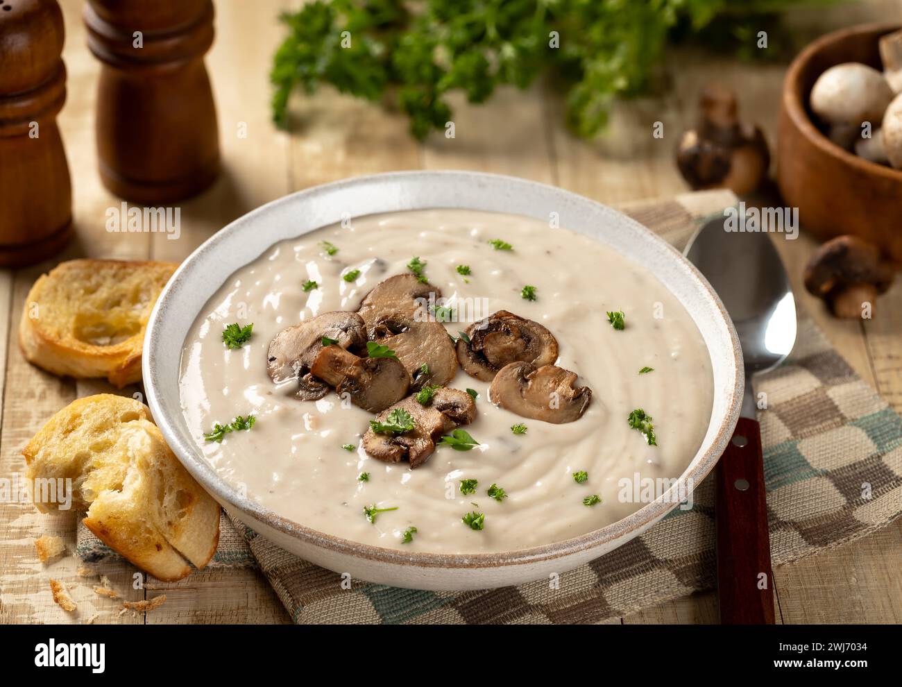 Schüssel cremige Pilzsuppe mit Pilzscheiben, Petersilie und gerösteten Baguettes auf einem rustikalen Holztisch Stockfoto