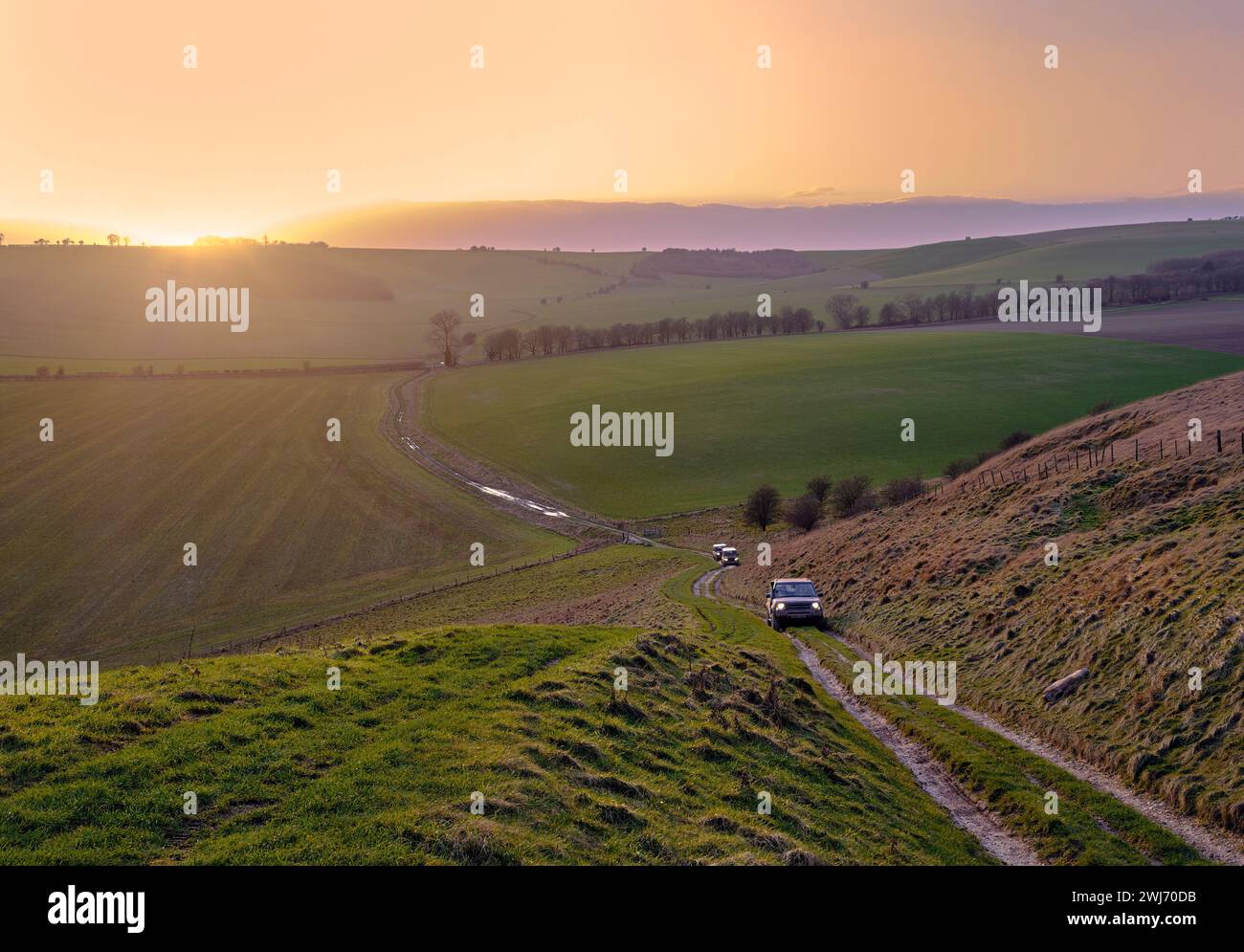 Land Rover klettern auf einer Nebenstraße zum Sugar Hill in den Marlborough Downs bei Sonnenuntergang. Wiltshire, England. Stockfoto