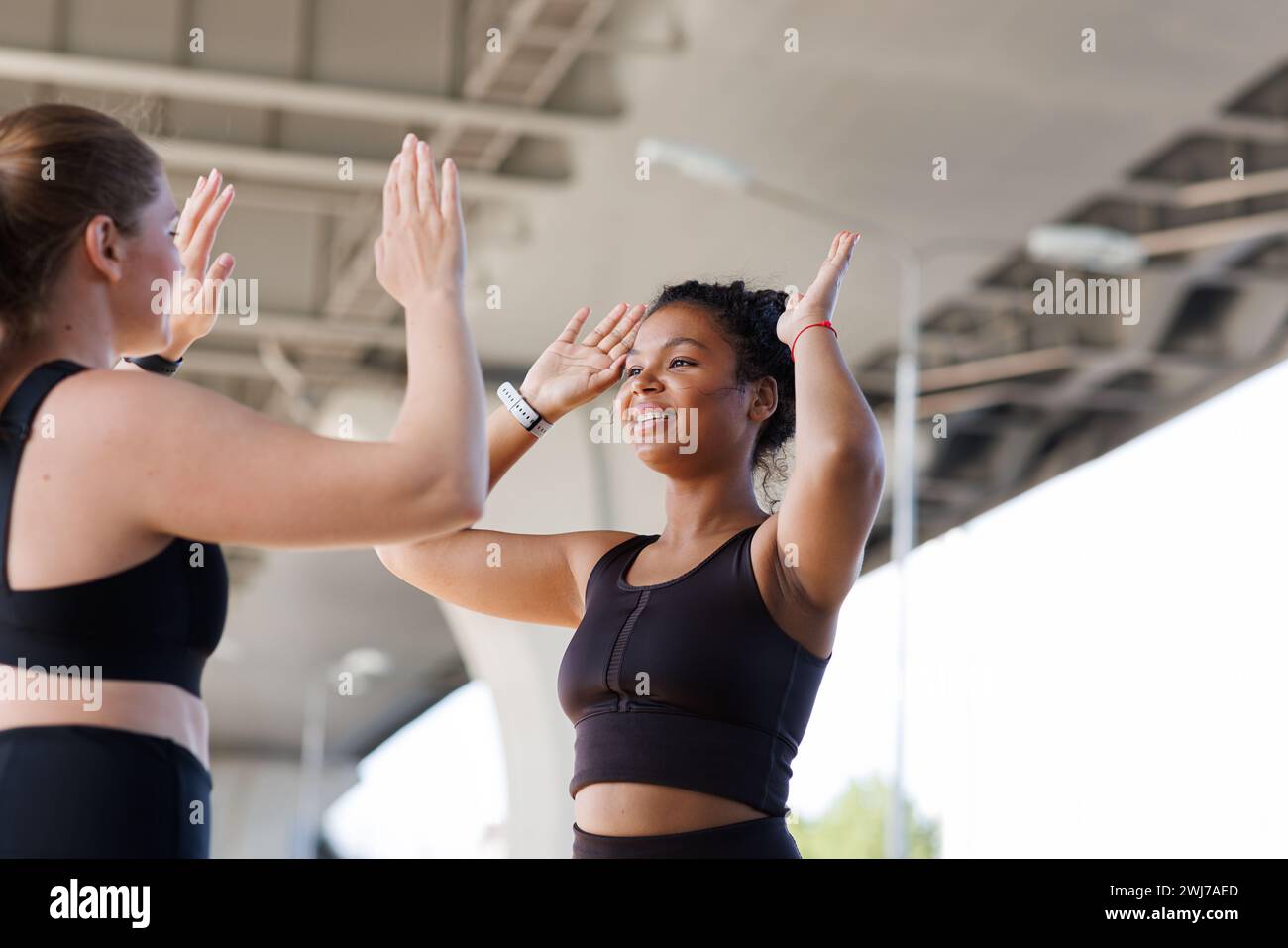 Junge lächelnde Frau, die ihrem Fitness-Kumpel fünf gibt. Zwei Frauen in Übergröße geben sich nach einem intensiven Workout im Freien High-Five. Stockfoto