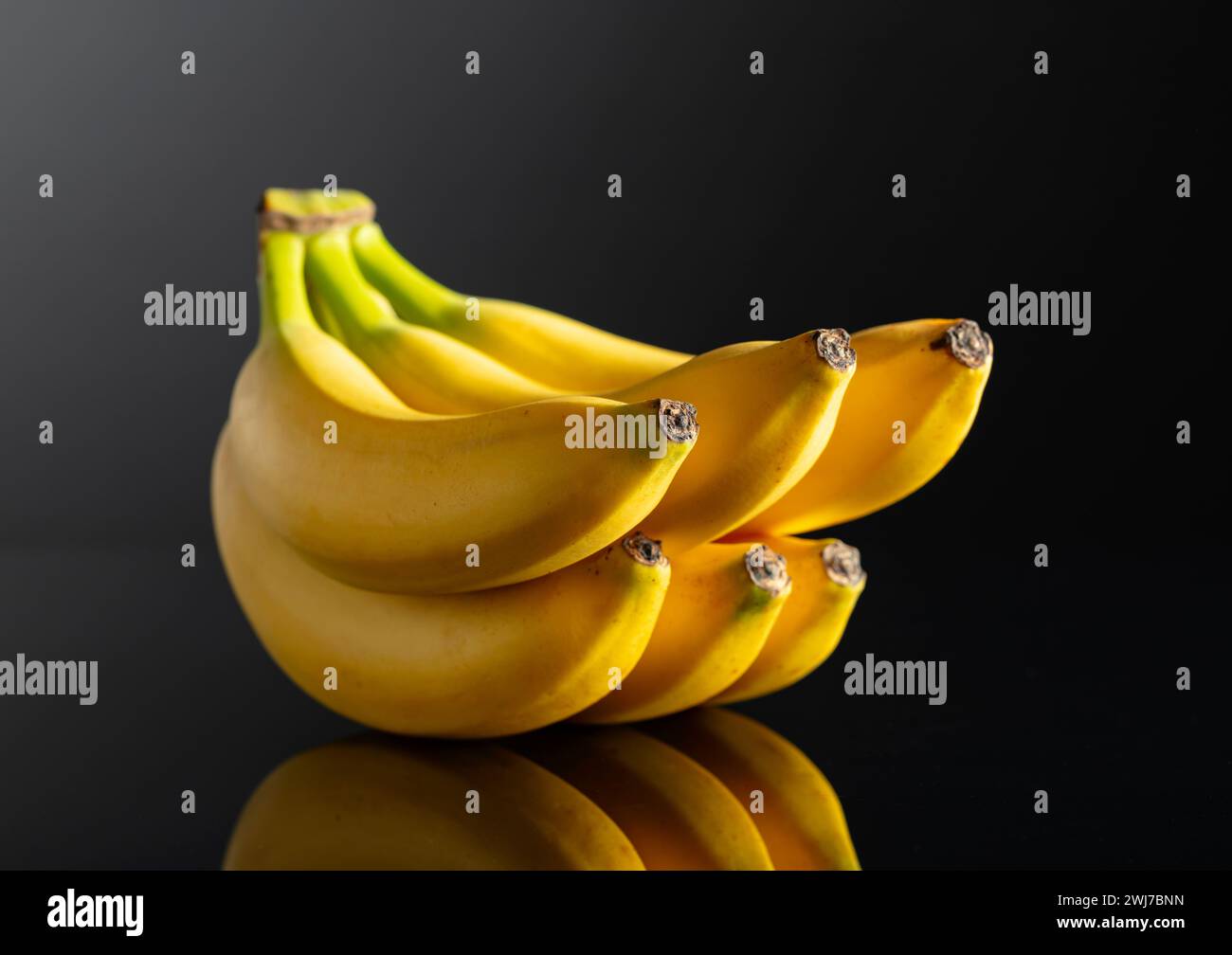 Ein Haufen reifer Bananen auf schwarzem reflektierendem Hintergrund. Stockfoto