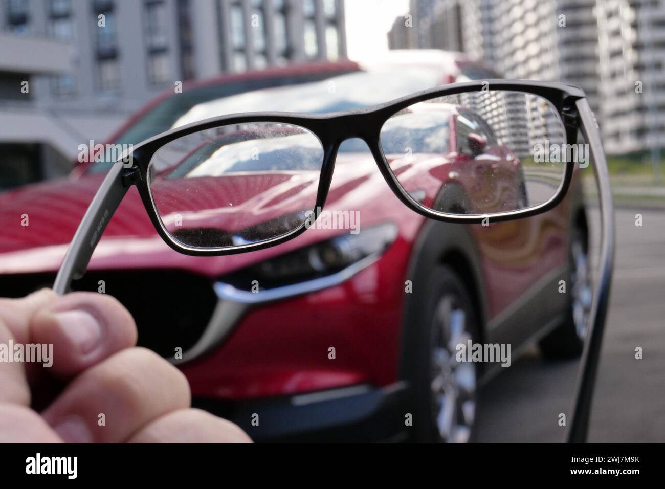 Konzeptfoto über schlechte Sicht des Fahrers bei unscharfem Fahrzeug ist in einer schmutzigen Brille in der menschlichen Hand zu sehen Stockfoto