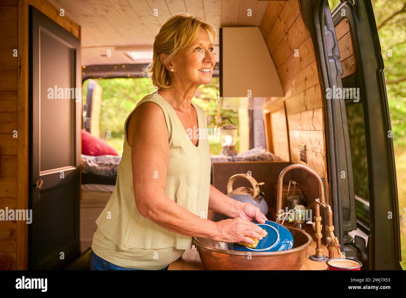 Seniorin genießt Camping auf dem Land, entspannend im Wohnmobil und erledigt Hausaufgaben Stockfoto