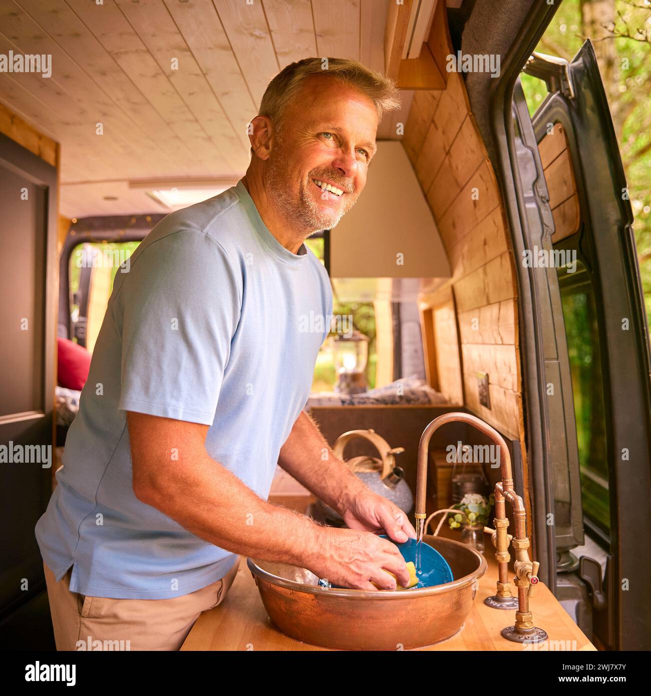 Senior Mann, der Camping auf dem Land genießt, sich im Wohnmobil zu entspannen und Hausaufgaben zu erledigen Stockfoto