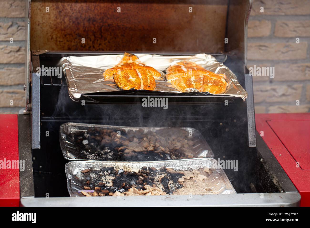 Nahaufnahme einer Außenküche mit offener Klappe, die frische Wildlachssteaks zeigt, die mit Apfelholz und Eichenholz geraucht werden Stockfoto