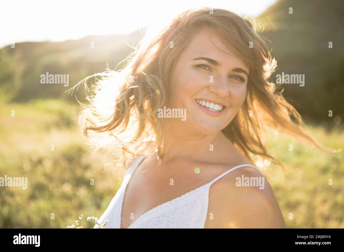 Lächelnde Frau mit fliegenden Haaren bei Sonnenuntergang im Sommer Stockfoto
