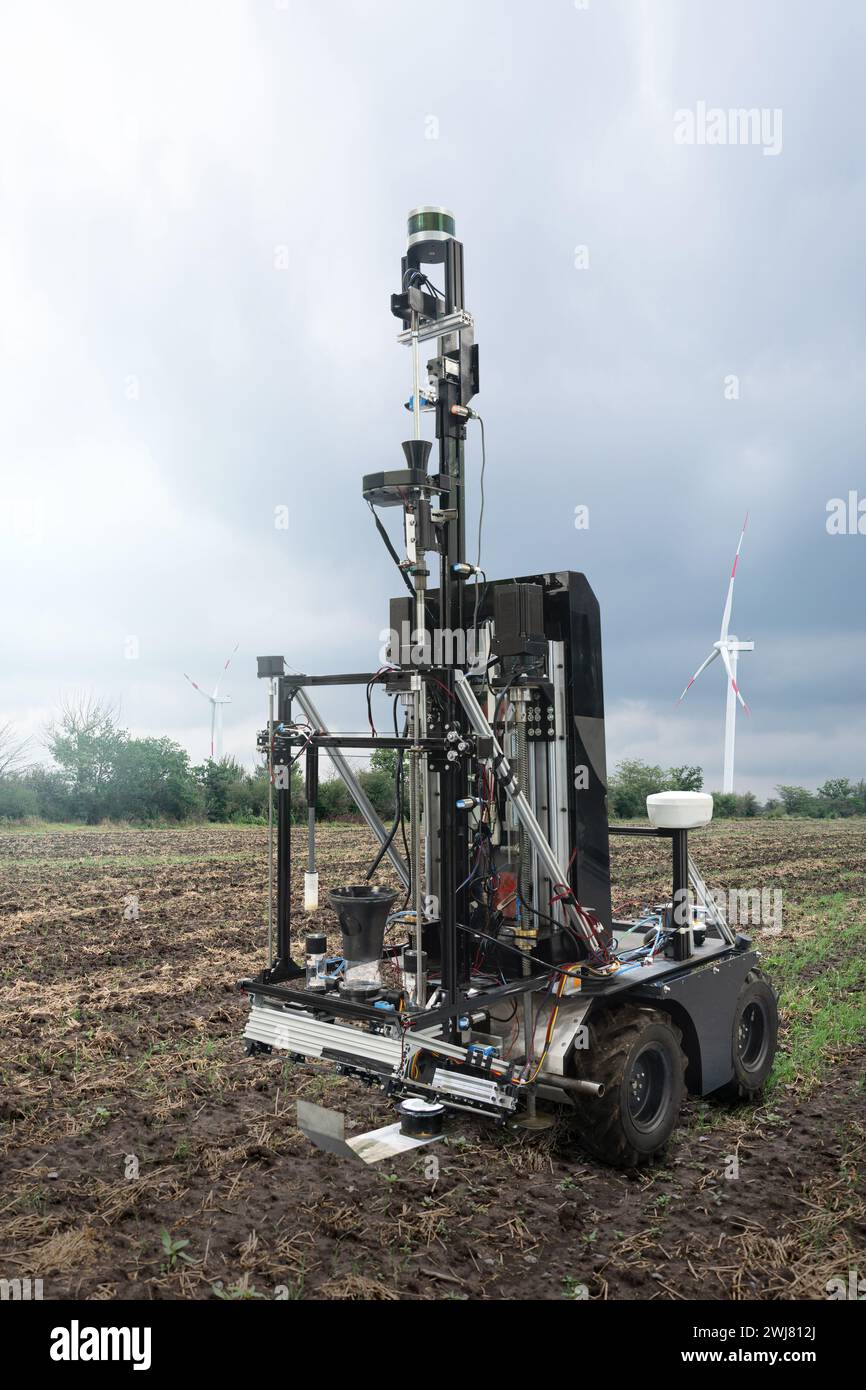 Autonomer Roboter zur Messung der Bodenqualität auf einem landwirtschaftlichen Feld. Windturbine am Horizont. Konzept der intelligenten Landwirtschaft. Stockfoto