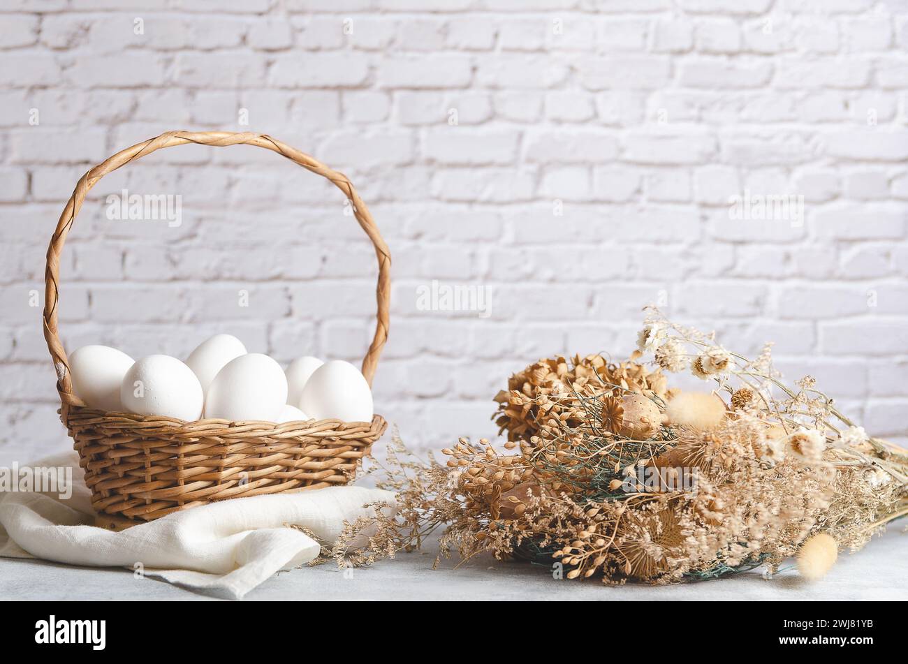 Ein Korb mit weißen Hühnereiern auf hellem Hintergrund mit getrockneten Blumen. Vorderansicht mit Kopierraum. Stockfoto