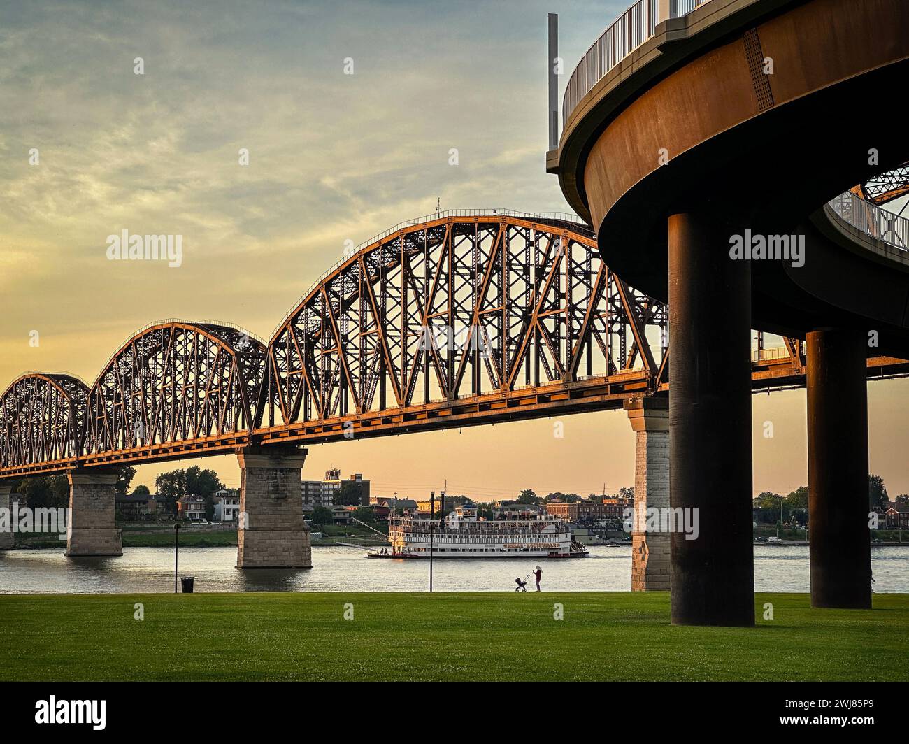 Das Flussboot Belle of Louisville schwimmt während des Sonnenuntergangs unter der Big Four Bridge auf dem Ohio River in Louisville, Kentucky, USA. Stockfoto