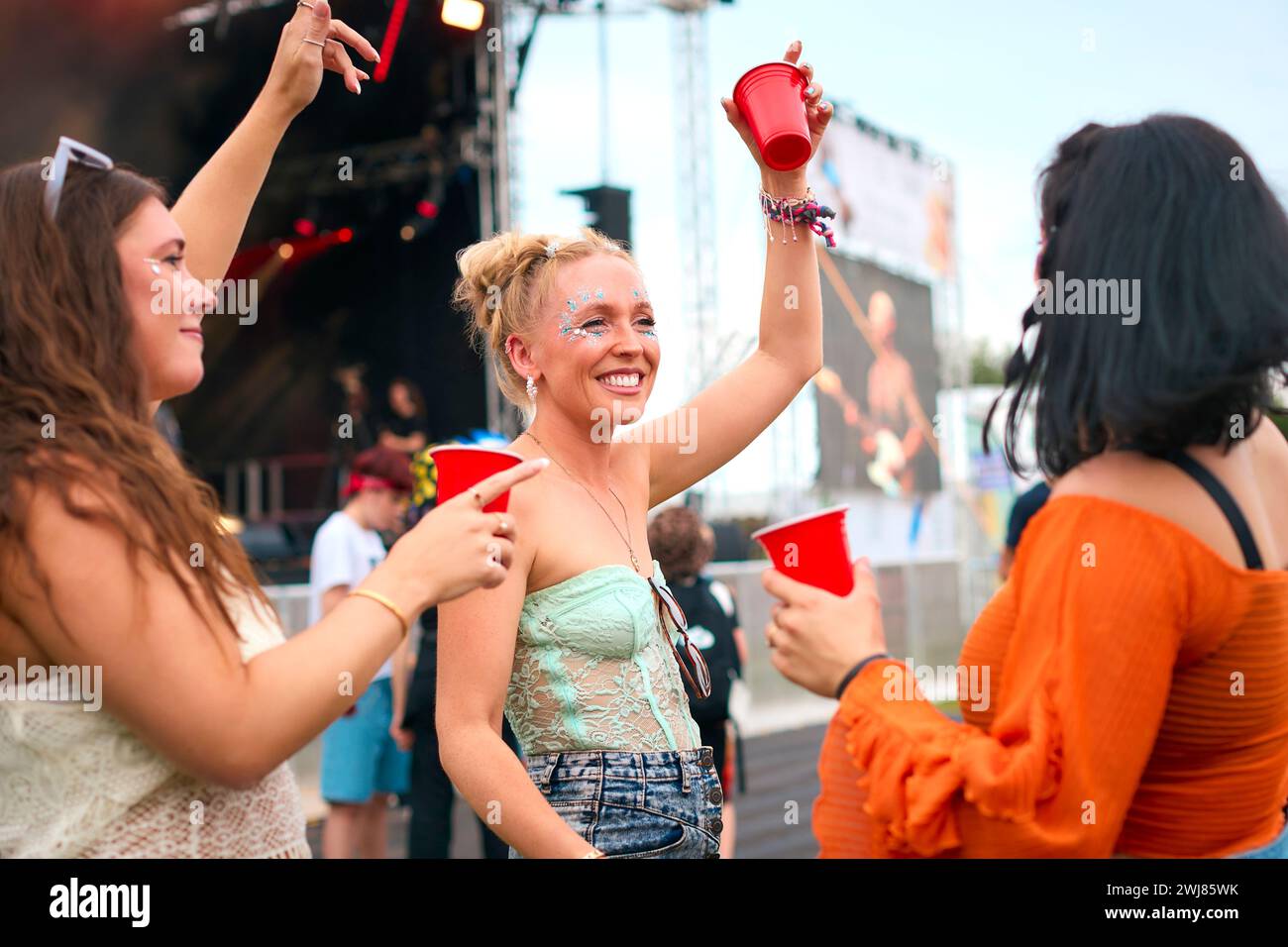 Drei Weibliche Freunde Mit Glitzer, Die Beim Summer Music Festival Spaß Haben Und Getränke Halten Stockfoto