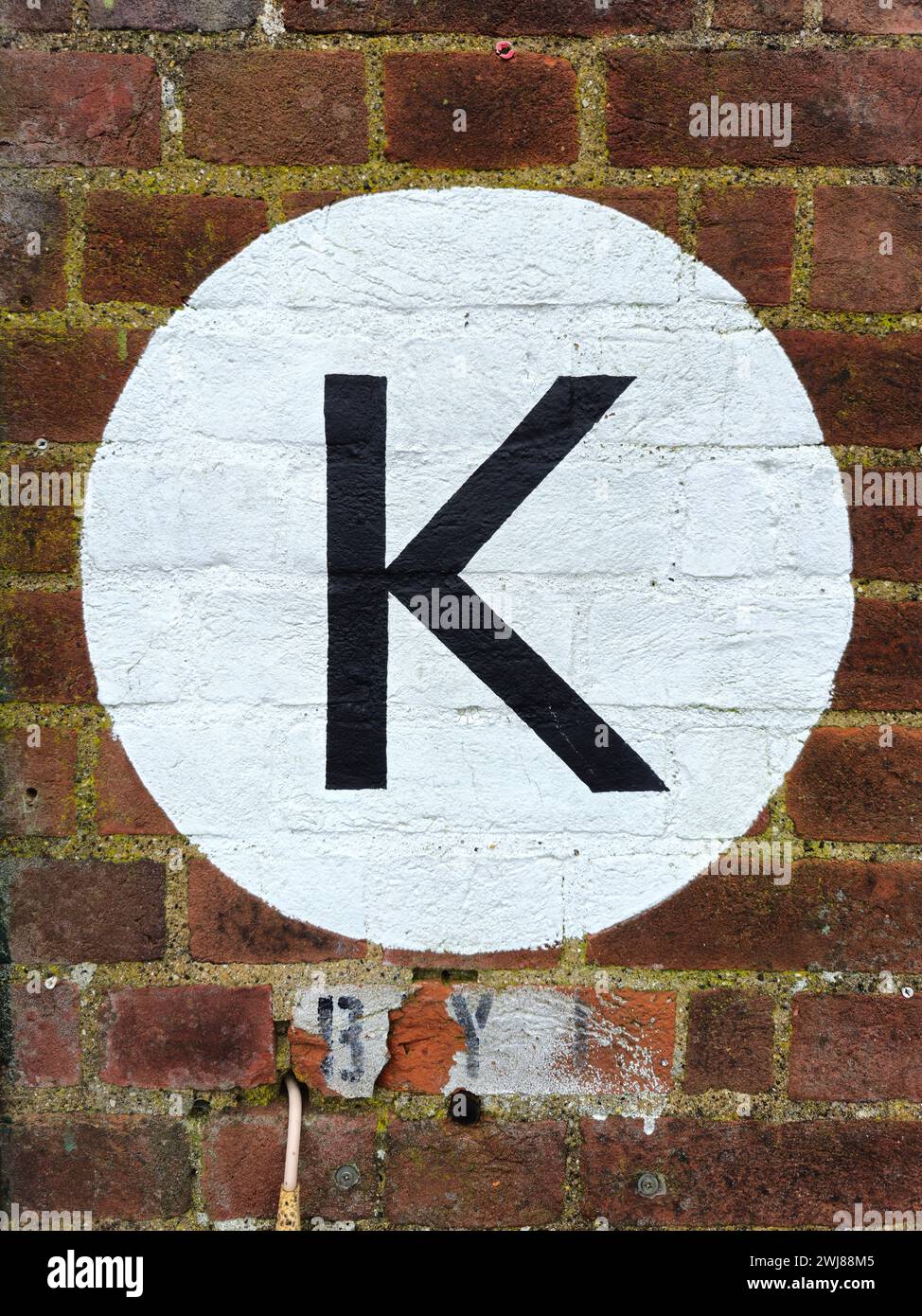 Schwarzer Buchstabe K, gemalt auf einem weißen Kreis an einer Ziegelwand Stockfoto