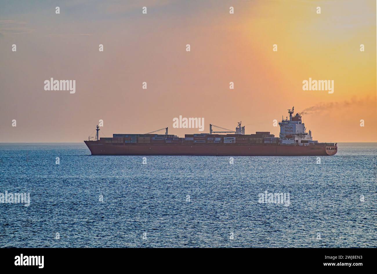 Panamakanal, Panama - 24. Juli 2023: Großes Containerschiff, roter Rumpf, hohe Ladung, wartet auf dem Pazifik im Morgenlicht auf blauem Wasser Stockfoto