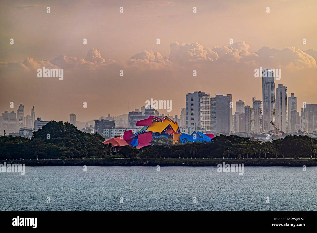Panamakanal, Panama - 24. Juli 2023: Nahaufnahme farbenfrohes Biodiversitätsmuseum am Eingang in nebeliger Morgenwolkenlandschaft. Stadtbild hinter, grüner Baum Stockfoto
