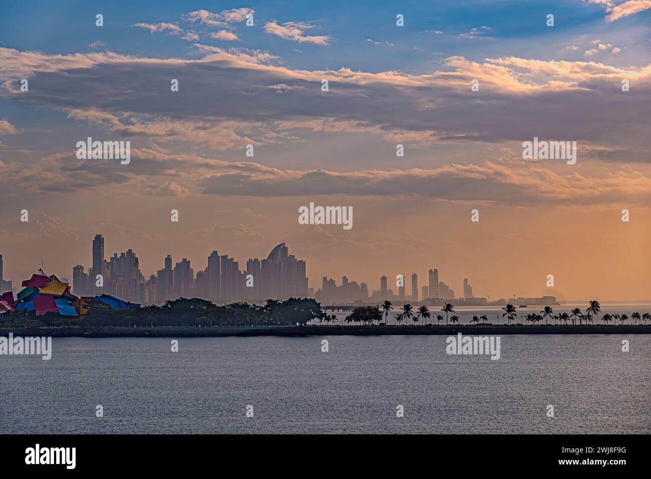 Panamakanal, Panama - 24. Juli 2023: Stadtbild hinter farbenfrohem Biodiversitätsmuseum am Eingang in nebeliger Morgenorange Wolkenlandschaft. Grüner Baumgürtel an Stockfoto