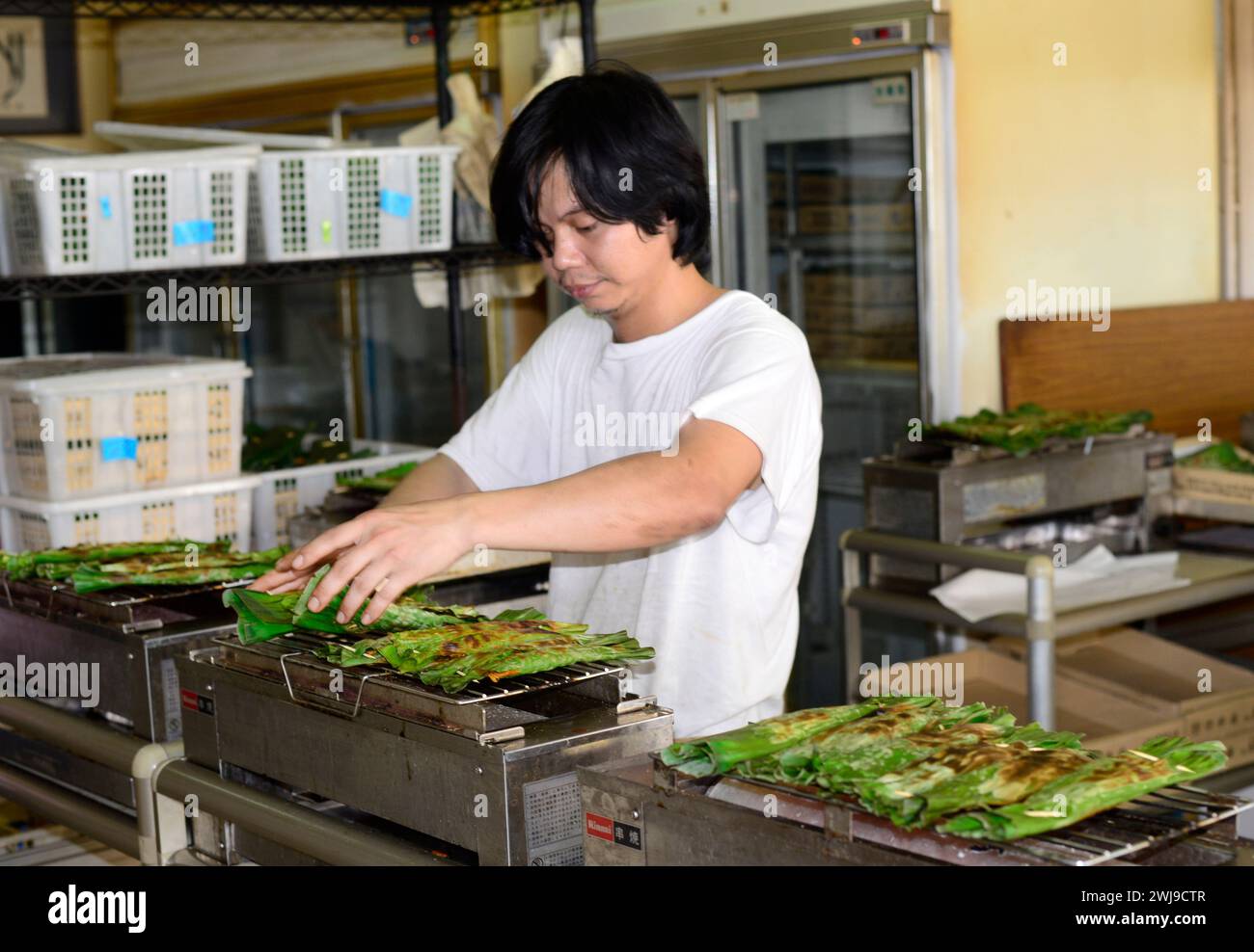 Ein Mann, der Otak-Otak grillt, einen südostasiatischen Fischkuchen, in Bananenblatt gewickelt. Stockfoto