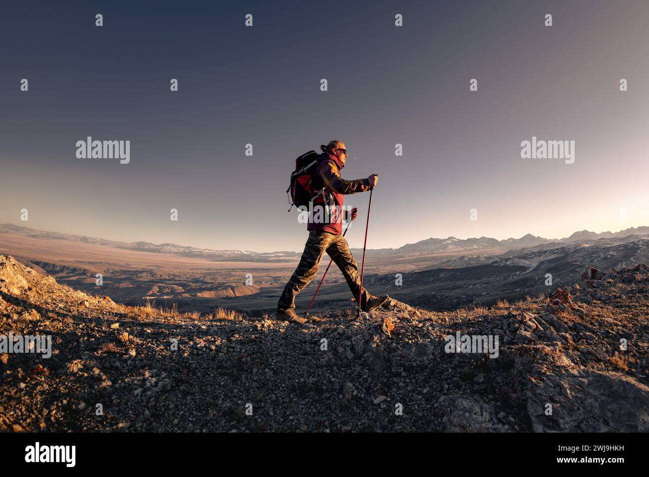 Wanderer mit Rucksack spaziert hoch in den Bergen bei Sonnenuntergang Stockfoto