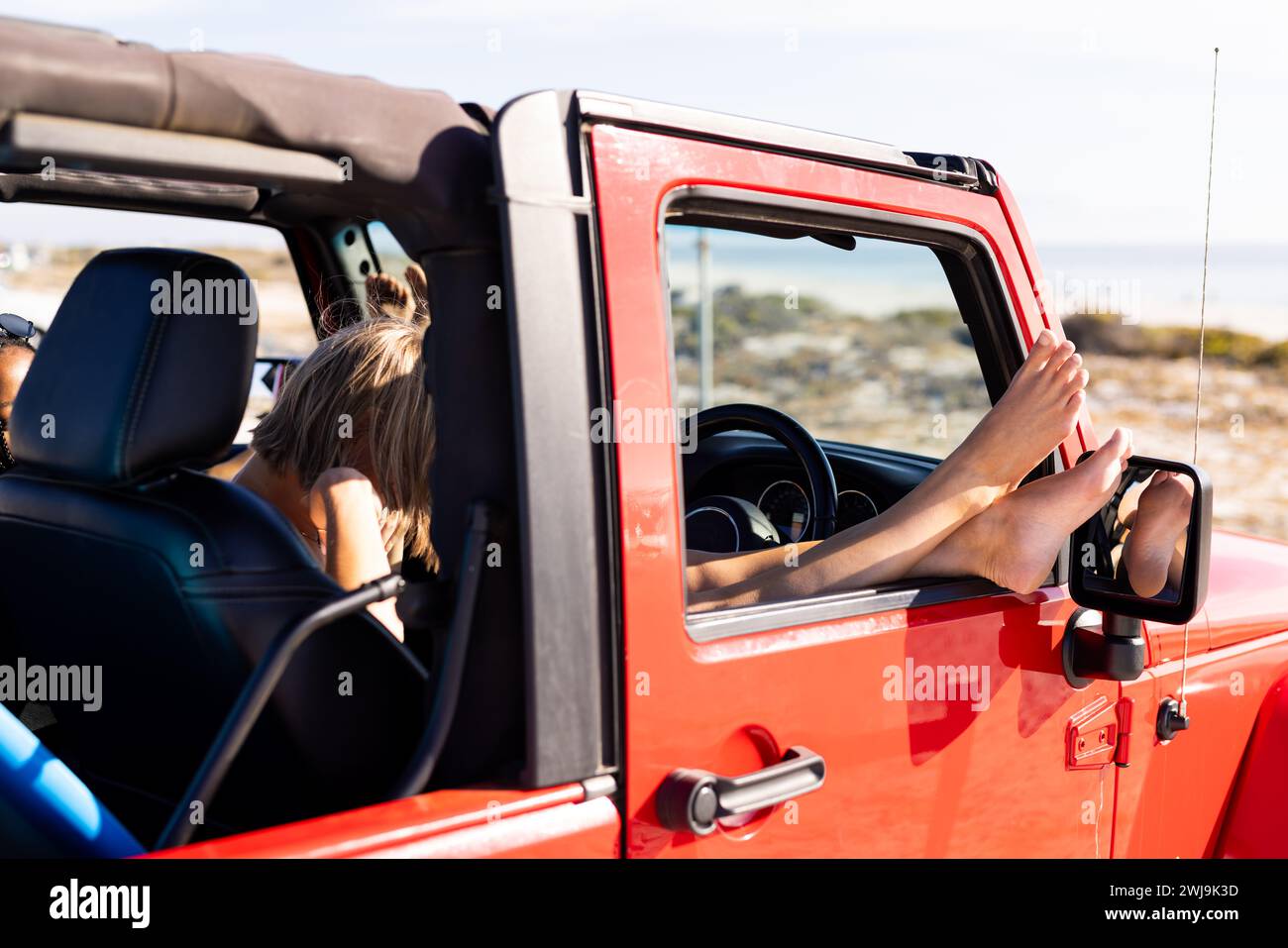 Die junge kaukasische Frau genießt eine sonnige Fahrt in einem roten Cabrio auf einem Roadtrip Stockfoto