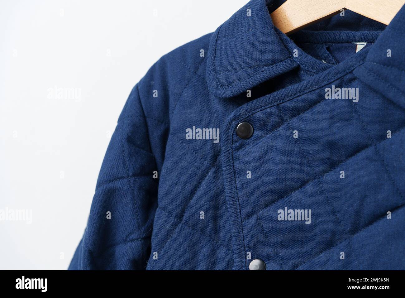 Blauer gesteppter Kindermantel am Aufhänger an der weißen Wand Stockfoto
