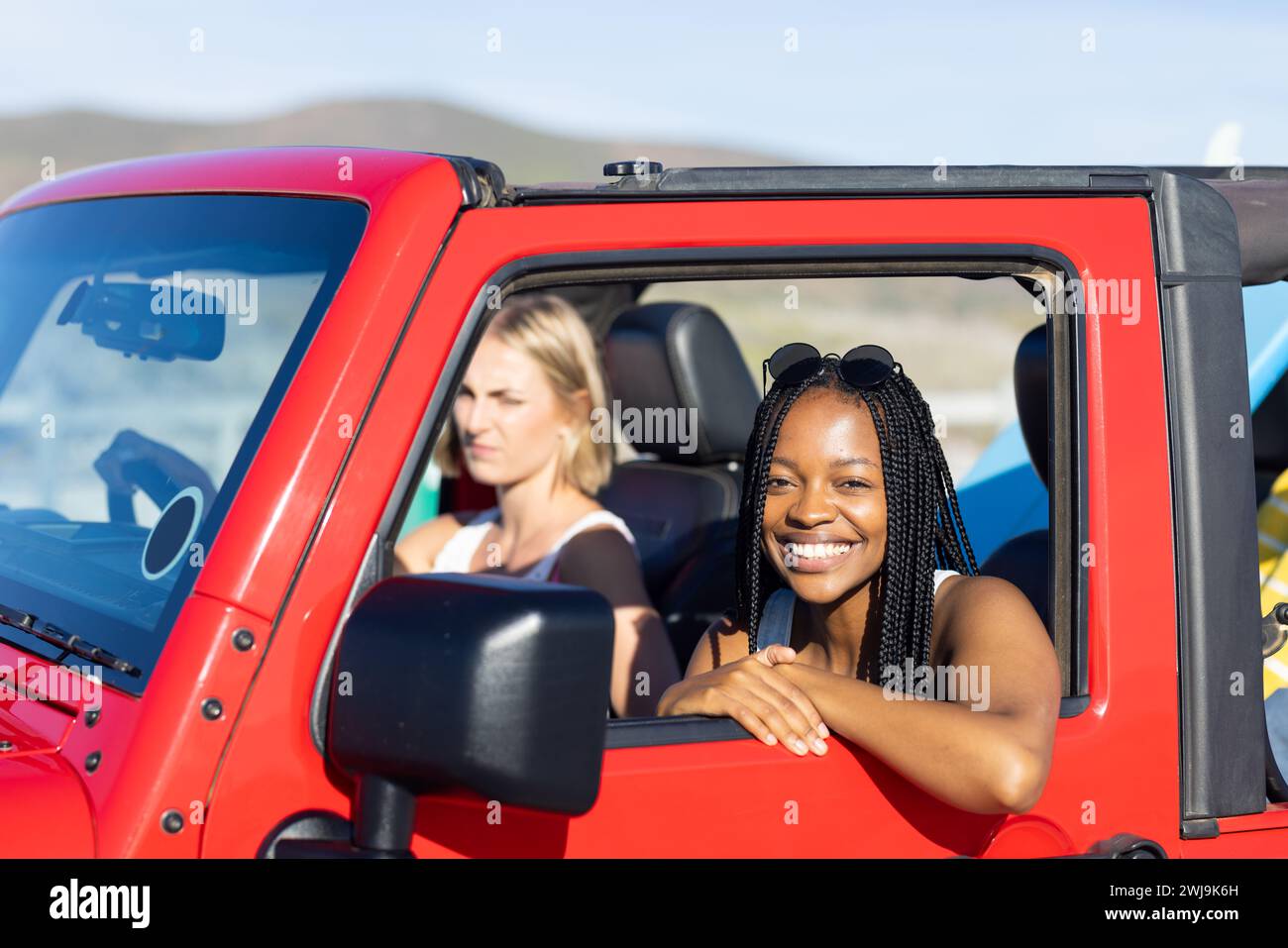 Junge afroamerikanische Frau und junge kaukasische Frau genießen eine sonnige Fahrt auf einem Roadtrip Stockfoto