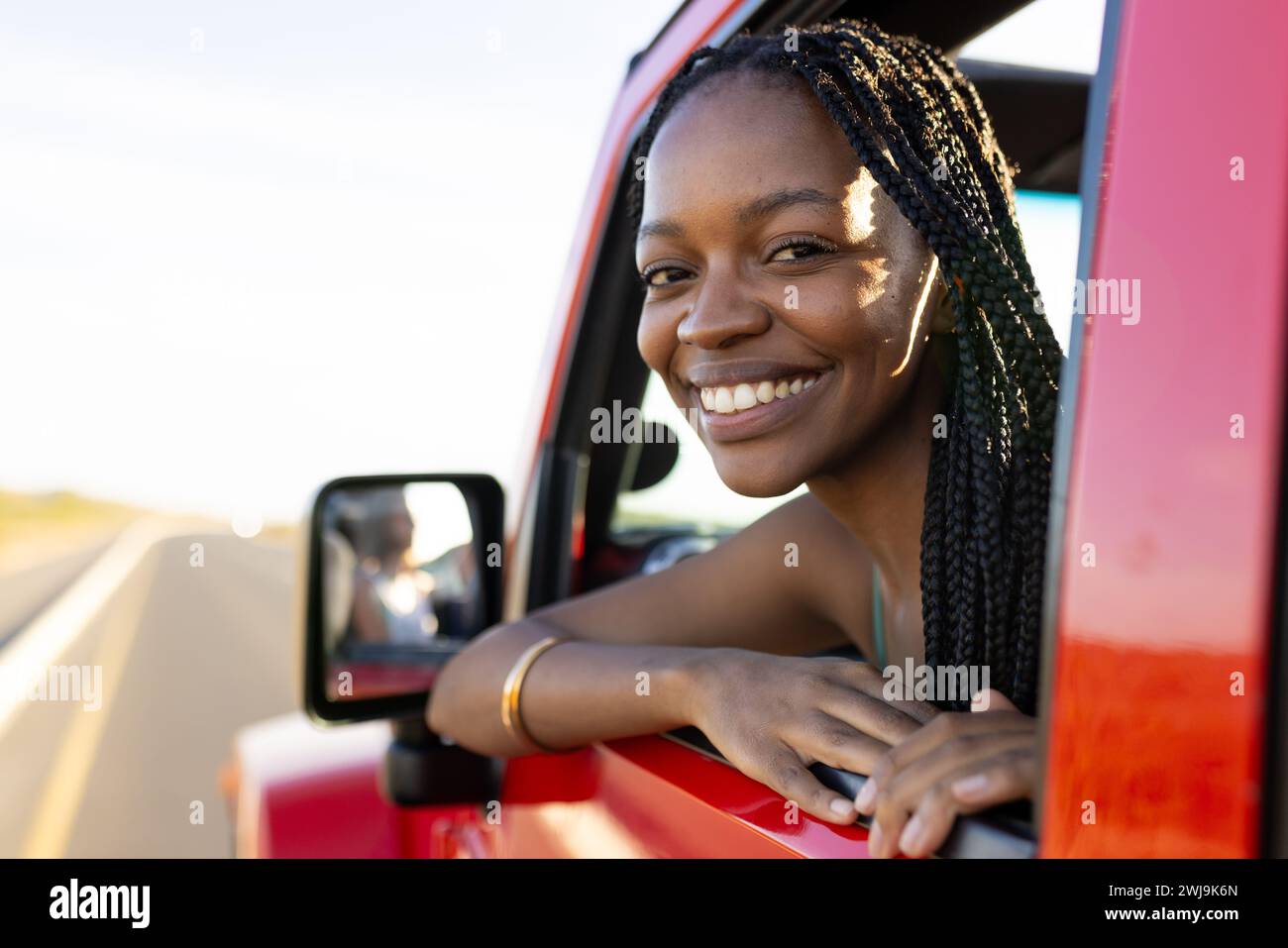 Die junge afroamerikanische Frau lächelt von einem roten Fahrzeug auf einer Reise, mit Kopierraum Stockfoto