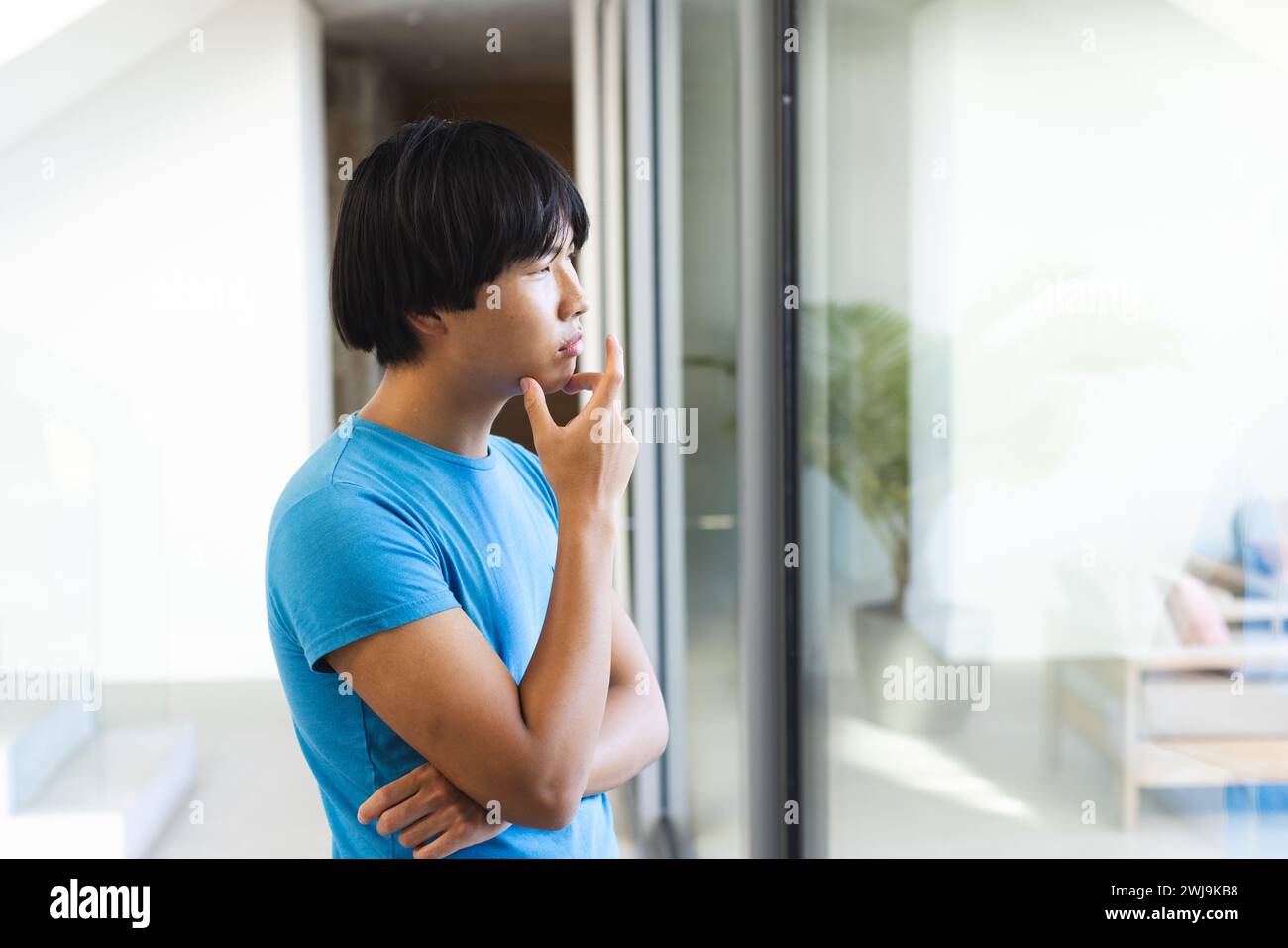 Der asiatische Teenager schaut nachdenklich vor einem Fenster zu Hause Stockfoto