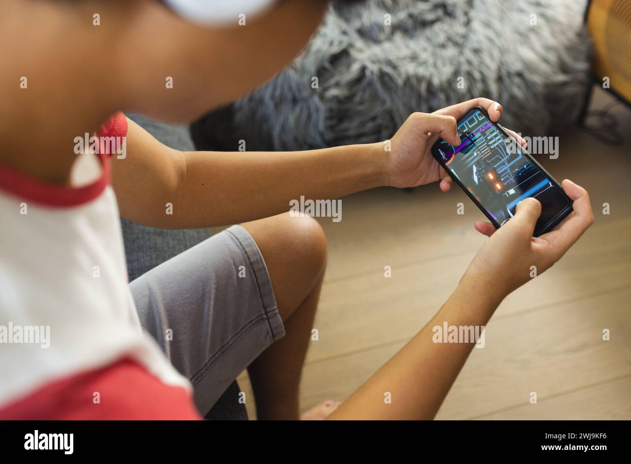 Der Teenager asiatische Junge hat sich darauf konzentriert, ein Spiel auf seinem Smartphone zu Hause zu spielen, mit Kopierraum Stockfoto