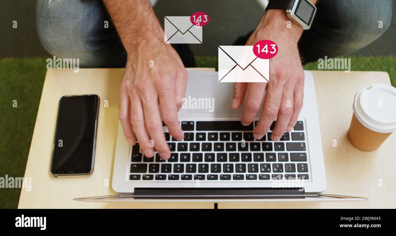 Mann tippt auf Laptop mit aufsteigenden E-Mail-Symbolen, Telefon und Kaffee neben ihm in 4k. Stockfoto