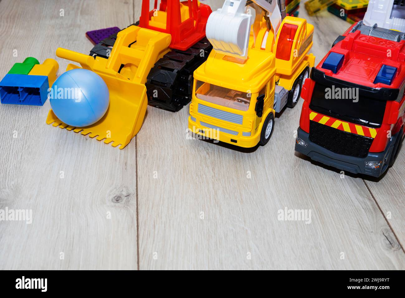 Kinderspielzeugautos aus Kunststoff, ein Feuerwehrauto, ein Bagger, ein Traktor, sind auf dem Boden Stockfoto