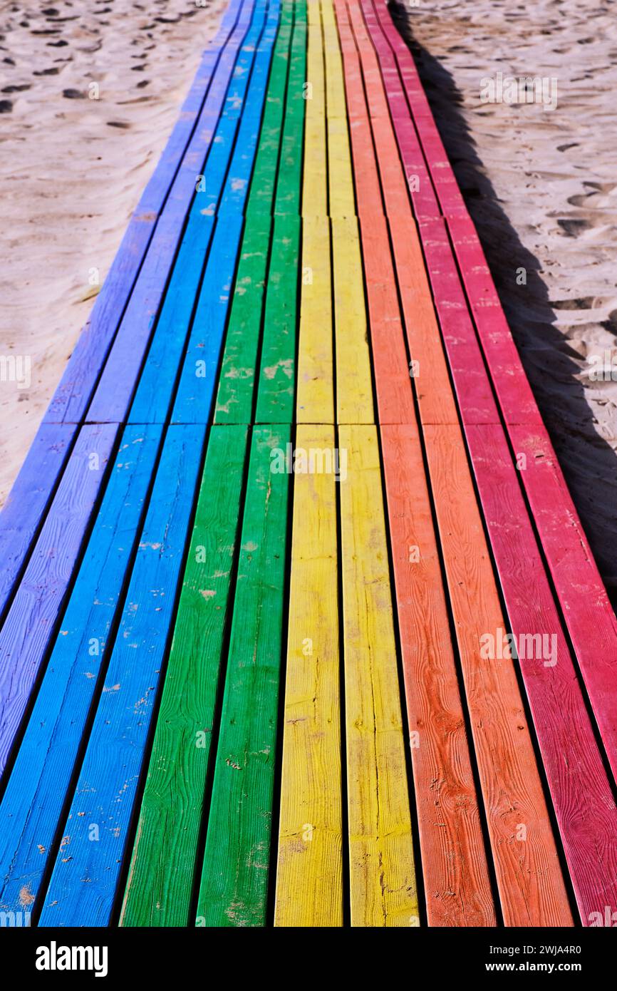 Holzweg zum Strand mit blauen grünen gelben orange und roten Farben an der Sandküste am sonnigen Tag in Penon de Ifach in Calpe, Alicante, Spanien Stockfoto