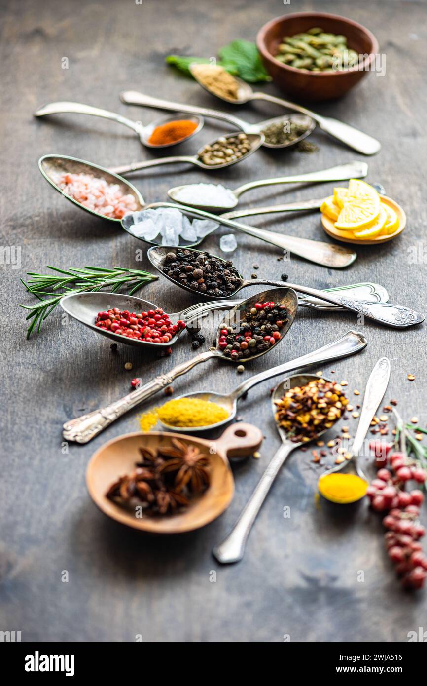 Verschiedene Gewürze und Samen, darunter Sonnenblumenkerne, Anissterne und Rosmarin, kunstvoll in Löffeln auf einer strukturierten Oberfläche mit Zitronenscheiben angeordnet Stockfoto