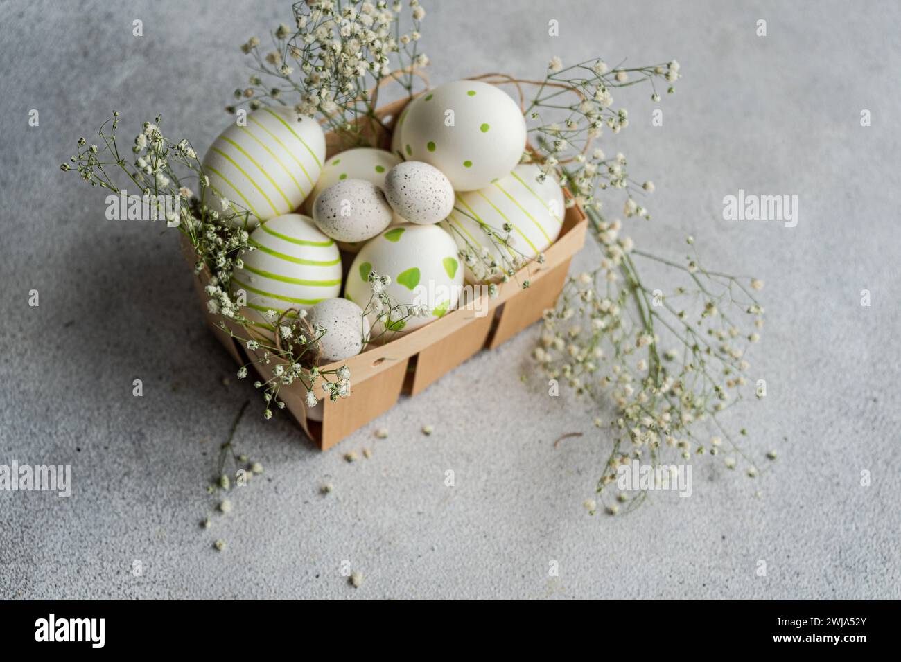 Eine bezaubernde Sammlung bemalter Ostereier mit Streifen und Punkten, eingebettet in einen Korb mit zarten Frühlingsblumen Stockfoto