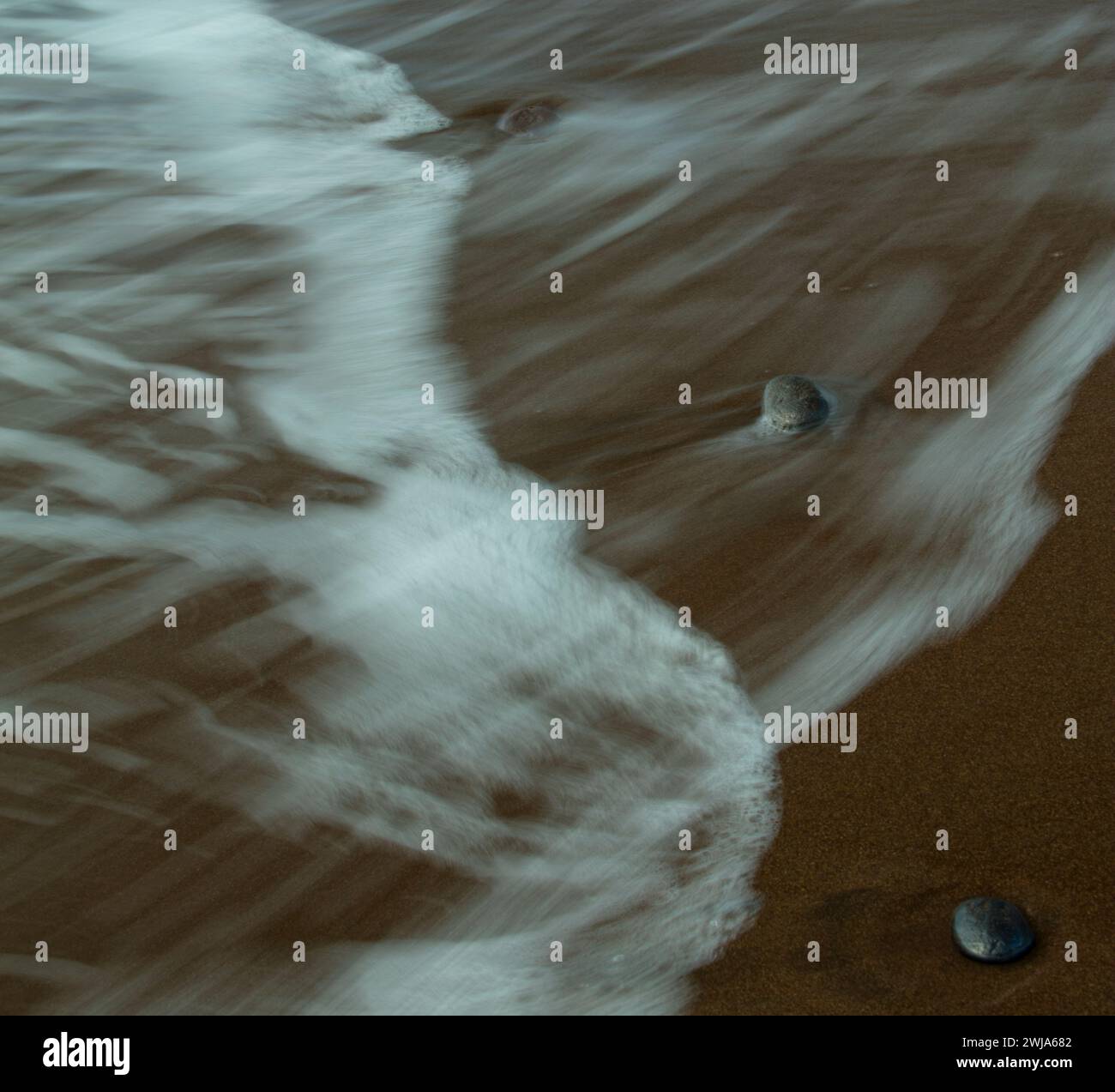 Ruhige Strandszene mit sanften Wellen über Sandstrand und Felsen Stockfoto