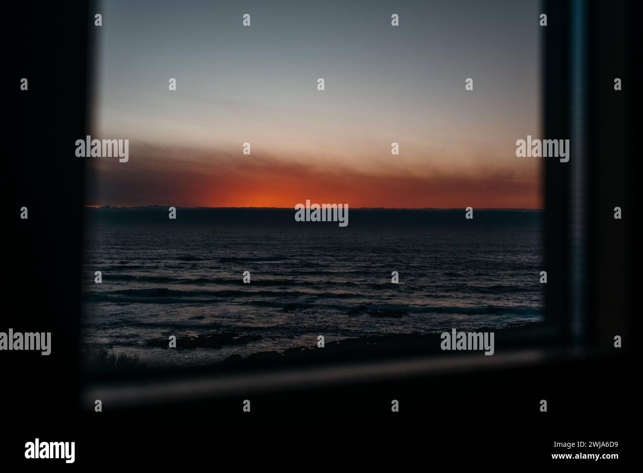 Ruhiger Sonnenuntergang über dem Meer, eingerahmt von der Silhouette eines Fensters, von einem gemütlichen Aussichtspunkt in Larino, Galicien, Spanien. Stockfoto