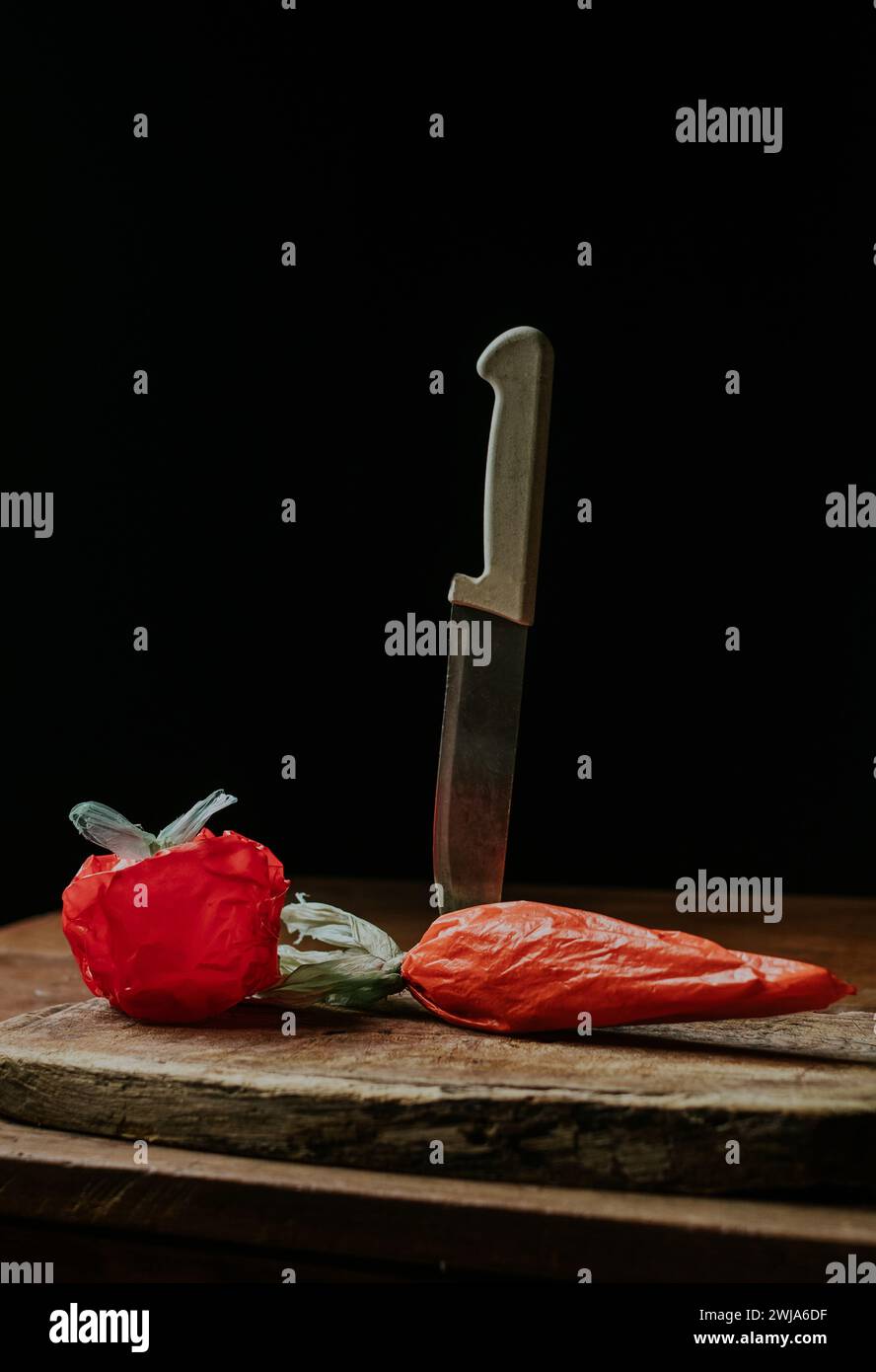 Plastiktüten, die an eine Tomate und Karotte erinnern, neben einem Küchenmesser auf einem rustikalen Holzschneidebrett Stockfoto