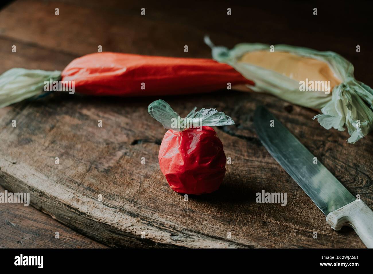 Plastiktüten in Form einer Tomate, Karotte und Paprika neben einem Messer auf einer alten Holzoberfläche Stockfoto