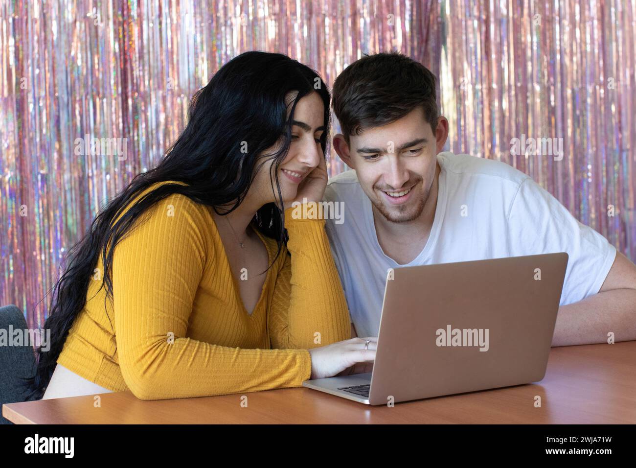 Glücklicher bärtiger Mann, der neben einer lächelnden jungen Frau sitzt und einen Laptop benutzt und auf den Bildschirm im Zimmer blickt Stockfoto