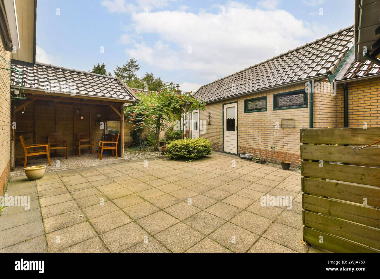 Ein privater Hinterhof mit überdachter Terrasse, Sitzgelegenheiten im Freien, Pflastersteinen und einem gepflegten Garten. Stockfoto
