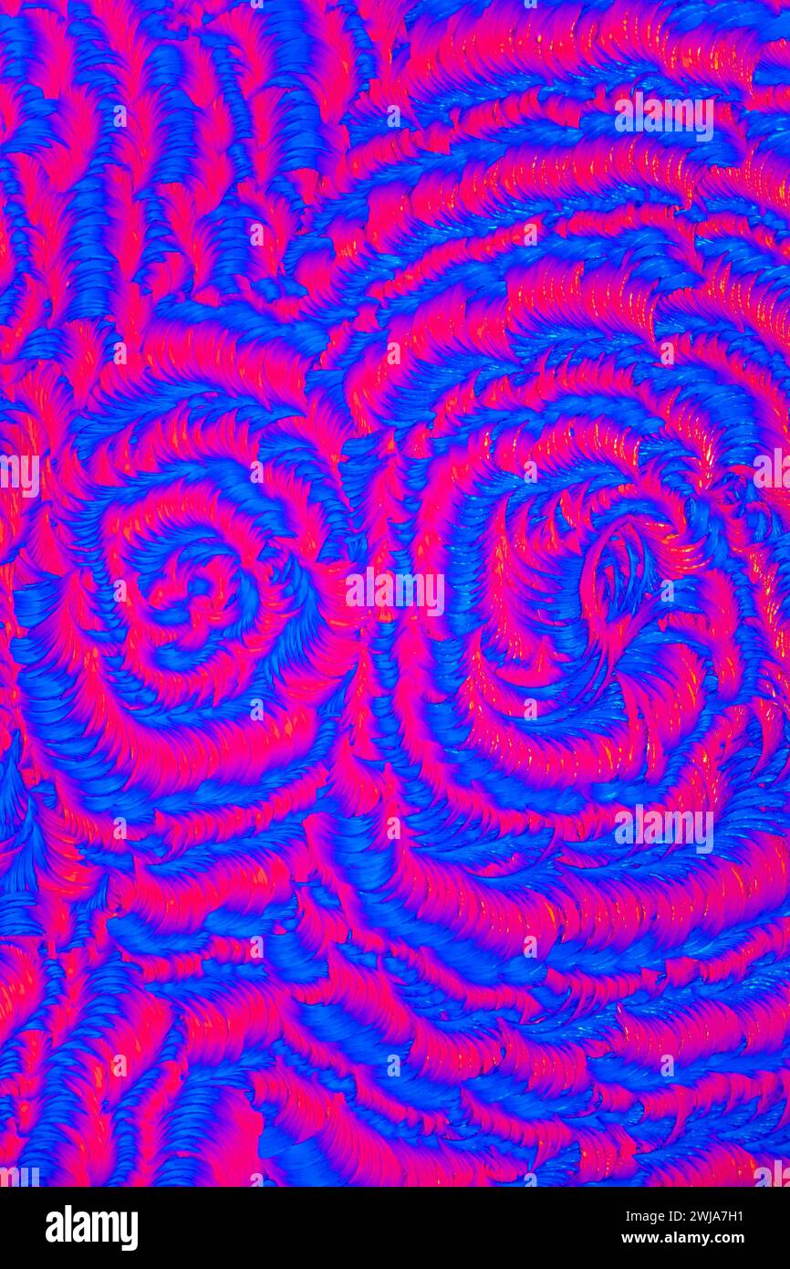 Lebendige blaue und rote Salicylsäure-Kristallmuster, die unter einem Mikroskop erfasst werden und einen hypnotischen Spiraleffekt erzeugen Stockfoto