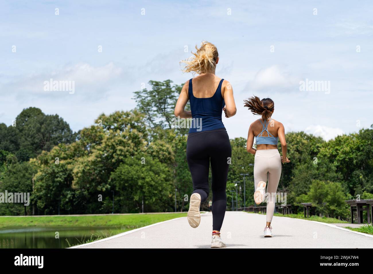 Voller Körper anonymer junger Frauen in Aktivkleidung und Turnschuhen, die während des Cardio-Workouts in der Nähe von Büschen in Thailand Chiang Mai auf der Straße joggen Stockfoto